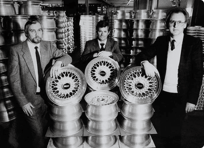 The founders of BBS standing with stacks of forged wheels.
